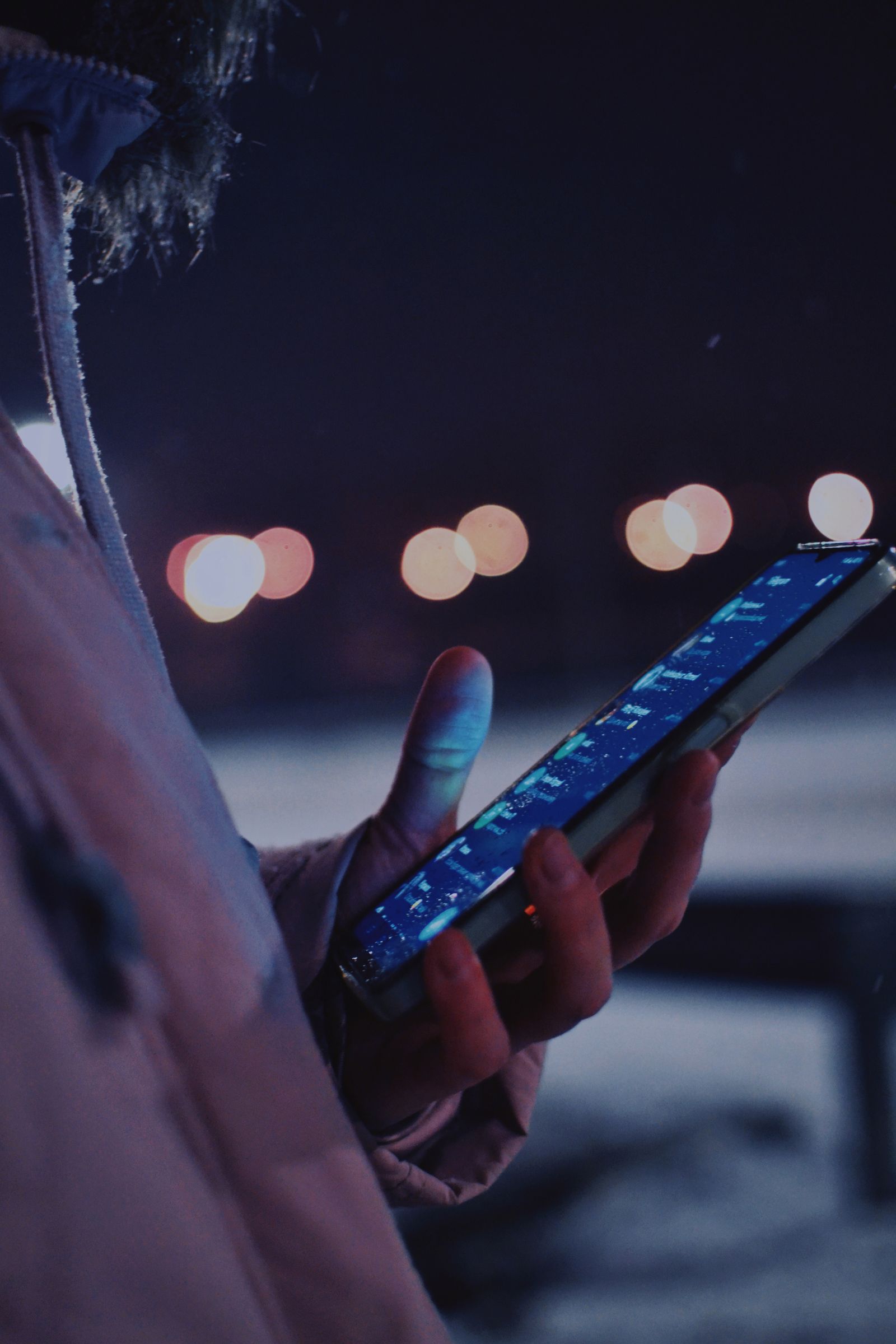 Mano usando un smartphone de noche con luces de la ciudad desenfocadas